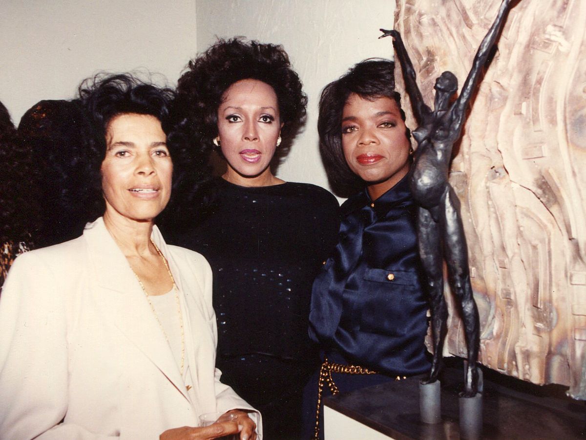 Three women standing next to a statue of a woman.
